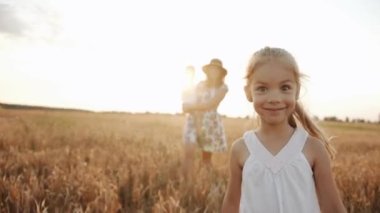 Ön dişleri eksik bir kız kameraya yüzünü buruşturuyor ve annesi buğday tarlasında kucağında küçük bir oğluyla oturuyor. Yavaş çekim