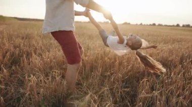 Sakallı genç bir adam mutlu kızını elinden ve bacağından tutup buğday tarlasında döndürür. Yavaş çekim