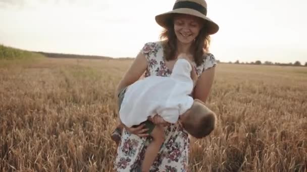 O tânără frumoasă într-un câmp de grâu își ține fiul în brațe și îl gâdilă. Slow motion — Videoclip de stoc