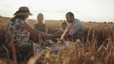 Çocuklu arkadaş canlısı bir aile güneşli bir yaz gününde buğday tarlasında piknik yaparken doğaçlama bir masanın etrafında oturur. Ağır çekim. Aile birlikte dua ediyor.
