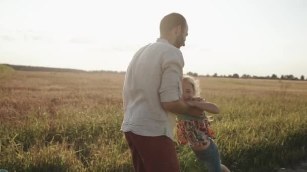 Молодий батько з бородою грає зі своїми дітьми в природі і кидає щасливу дочку в повітря — стокове відео