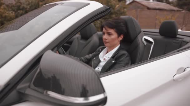 En vacker ung kvinna i svart skinnjacka kör en cabriolet på en landsväg och beundrar landskapet. Långsamma rörelser — Stockvideo