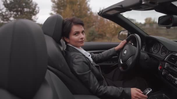 Uma jovem elegante senta-se ao volante de um luxuoso conversível e segura a mão na alavanca de engrenagem. Movimento lento — Vídeo de Stock