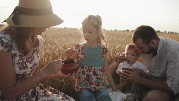Ung lycklig familj med barn vilar på en picknick på ett vetefält och äter god mat. Kärlek och omsorg — Stockvideo
