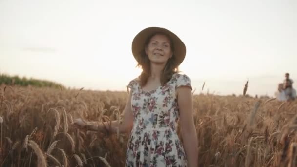 Uma jovem de chapéu de palha atravessa um campo de trigo ao sol dos raios. Conceito de privacidade e liberdade. Movimento lento. Visão traseira — Vídeo de Stock