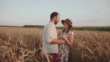 Genç evli bir çift buğday tarlasında sarılıp öpüşüyor. Aşk ve mutluluk kavramı. Yavaş çekim