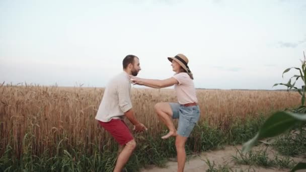 Couple heureux sur une promenade dans les champs et l'homme soulève la jeune femme riante dans le chapeau — Video