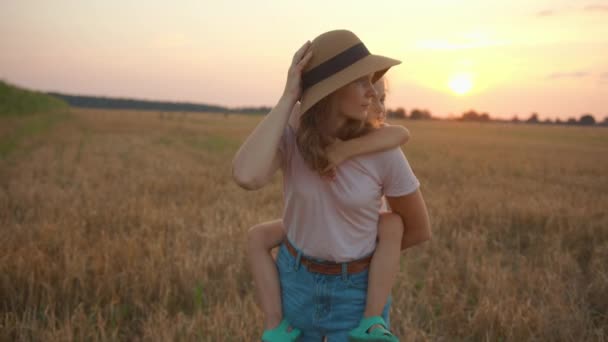 Uma bela jovem segura sua filha de costas enquanto está em um campo de trigo e a beija. Movimento lento — Vídeo de Stock