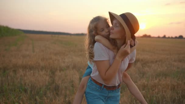 Una hermosa joven sostiene a su hija boca arriba mientras está de pie en un campo de trigo y la besa. Movimiento lento — Vídeo de stock
