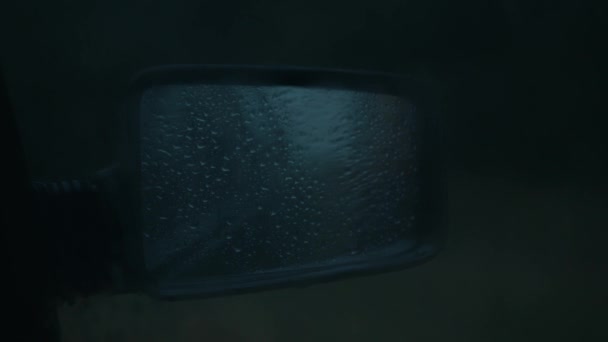 Крупный план бокового зеркала автомобиля с капельками дождя и размытым силуэтом человека, проходящего мимо — стоковое видео