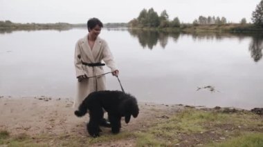 Kısa saçlı enfes bir genç kadın nehir kıyısında fino köpeğiyle yürüyor ve sıcak bir sonbahar gününün tadını çıkarıyor. Yavaş çekim