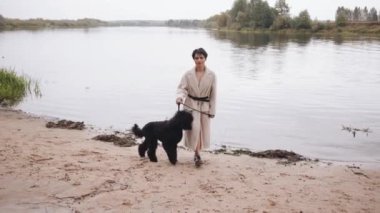 Kısa saçlı, çarpıcı genç bir esmer nehrin kumlu kıyısına gider ve büyük siyah bir kanişi tasmayla gezdirir. Yavaş çekim