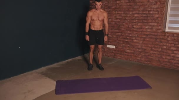 Pemuda berotot berolahraga di ruangan di atas tikar dan melakukan latihan ulat dengan melompat — Stok Video