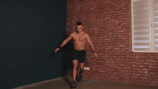 Młody mężczyzna z nagimi tułowia szkolenia w pokoju i robi skoków jack ćwiczenia i rzuca się do przodu — Wideo stockowe