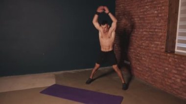 Siyah şortlu, tişörtsüz, evde antrenman yapan ve egzersiz yapan kaslı bir adam. Spor ve sağlıklı yaşam tarzı kavramı