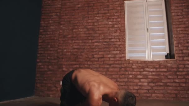 Ung kroppsbyggare i svarta shorts tränar på en matta inomhus och gör en armbåge planka med armarna utsträckta framåt — Stockvideo
