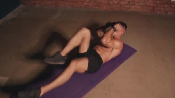 Bodybuilder utför intensiv intervallträning inomhus och uppfyller motionscykelsparkar när han ligger i båten poserar på mattan — Stockvideo