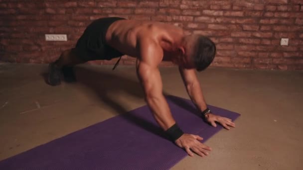 Hombre musculoso joven haciendo entrenamiento intenso en interiores sin equipo y bombeando músculos en sus brazos y espalda — Vídeos de Stock