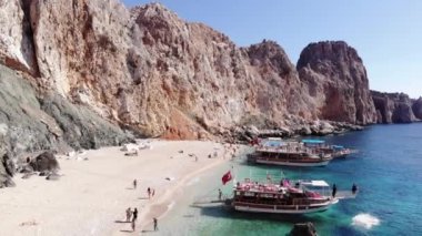 Türkiye, Kemer - 20 Ekim 2021: Suluada adasının volkanik kayaları ve körfezdeki yatlarla çevrili beyaz kumlu bir sahilde turistlerin insansız hava aracı vuruşu