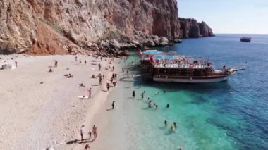 Türkiye, Kemer - 20 Ekim 2021: Suluada adasının volkanik kayalıkları ve açık turkuaz suyu ile körfez kıyısındaki birçok turistin havadan görüntüsü