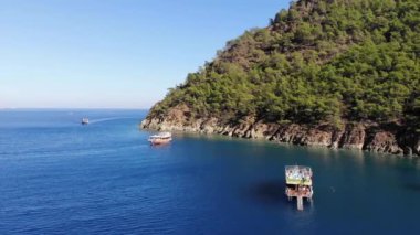 Türkiye, Kemer - 20 Ekim 2021: Koyun mavi sularında turistlerle yatların ve güneşli bir yaz gününde ağaçlarla kaplanmış kayalık adaların insansız hava araçlarıyla vurulması