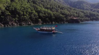 Ağaçlarla kaplı bir dağ adasının kıyısına yapılan gezi sırasında güvertede turistlerle birlikte bir yatın insansız hava aracı vurulması.