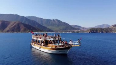 Türkiye, Kemer - 20 Ekim 2021: Açık mavi suyu ve dağ kıyısında bir grup turistle birlikte büyük bir yatın havadan görünüşü