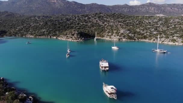 澄んだ青い水とアンタルヤ県の岩の山と地中海沿岸でヨットをセーリングと湾のドローン映像 — ストック動画