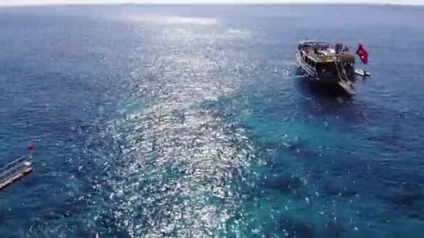 Turquia, Kemer - 20 de outubro de 2021: Vista aérea de iates com turistas em decks na superfície das águas claras do mar Mediterrâneo brilhando do sol — Vídeo de Stock