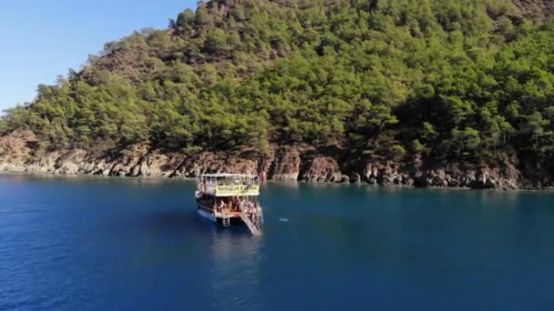 土耳其，凯末尔- 2021年10月20日：一架载有游客的游艇在布满树木的岩石岛屿附近的清澈蓝水中日光浴和游泳 — 图库视频影像