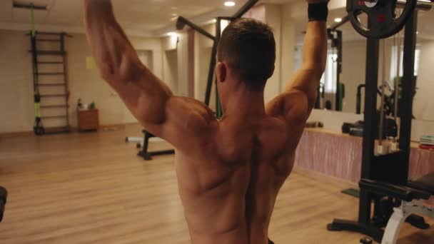 Close-up a parte de trás de um jovem homem musculoso no ginásio fazendo uma prensa de barra do peito sentado em um banco — Vídeo de Stock