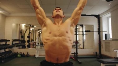 Genç vücut geliştirici spor salonunda çalışıyor halter ütülüyor ve omuz kemerinin kaslarını sallıyor.