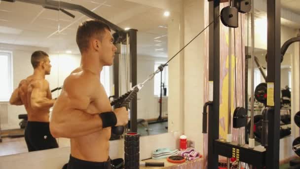 Um fisiculturista no ginásio e faz uma tração horizontal no peito no simulador de crossover para os músculos mais largos das costas e bíceps — Vídeo de Stock
