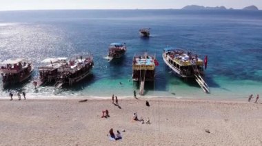 Türkiye, Kemer - 20 Ekim 2021: Suluada adasının beyaz kumlu plajında dinlenen turistlerin havadan görünüşü ve kıyı yakınlarındaki turkuaz denizde pek çok yat