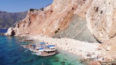 Suluada Adası 'ndaki turuncu volkanik dağların ve körfezde turist ve yatların bulunduğu beyaz plajın insansız hava aracı atışları.