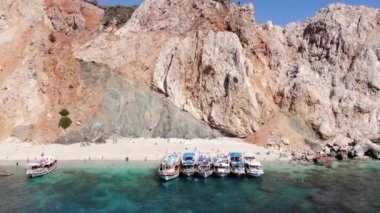 Suluada Adası 'ndaki turuncu volkanik dağların ve körfezde turist ve yatların bulunduğu beyaz plajın insansız hava aracı atışları.
