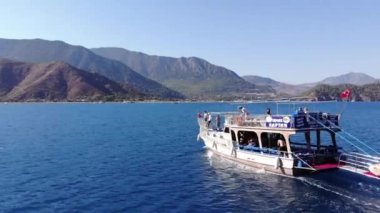 Türkiye, Kemer - 20 Ekim 2021: Açık mavi suyu ve dağ kıyısında bir grup turistle birlikte büyük bir yatın havadan görünüşü
