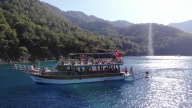 Türkiye, Kemer - 20 Ekim 2021: Açık mavi suyu ve dağ kıyısında bir grup turistle birlikte büyük bir yatın havadan görünüşü