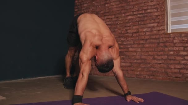발가벗은 몸통을 가진 젊은 근육질의 남자 가 집안에서 운동을 하고 팔을 들어 올려서 호흡 운동을 한다 — 비디오