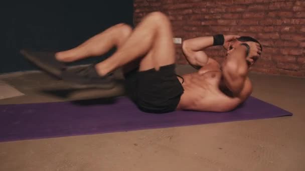 Giovane uomo con un busto nudo formazione nella stanza su un tappeto sportivo e fa un esercizio sulla stampa sdraiato in una posa barca — Video Stock