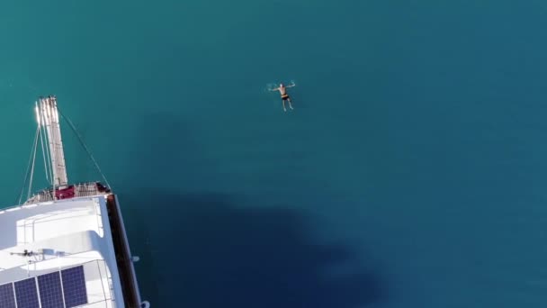Vue aérienne d'un homme qui flotte sur le dos dans les eaux turquoise de la mer près d'un yacht blanc avec des touristes — Video