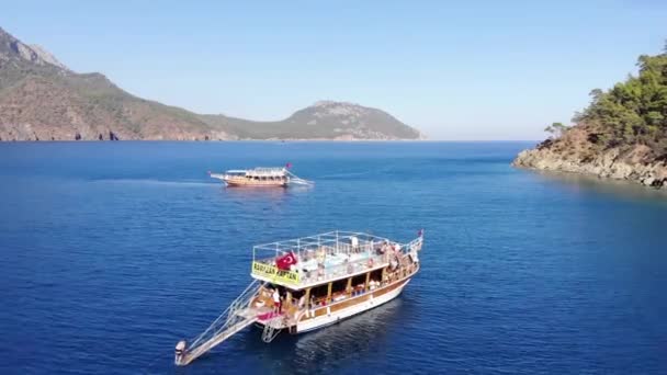 Türkei, Kemer - 20. Oktober 2021: Drohnenabschuss einer Jacht mit Touristen beim Sonnenbaden und Schwimmen im klaren, blauen Wasser in der Nähe einer mit Bäumen bedeckten Felseninsel — Stockvideo