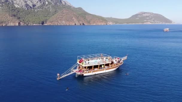 Turcja, Kemer - 20 października 2021: Drone strzelanie jachtu z turystami opalanie i pływanie w czystej niebieskiej wodzie w pobliżu skalistej wyspy pokrytej drzewami — Wideo stockowe