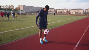 Formalı ve şortlu genç siyah kız stadyumun koşu pistinde futbol topuyla hokkabazlık yapıyor.