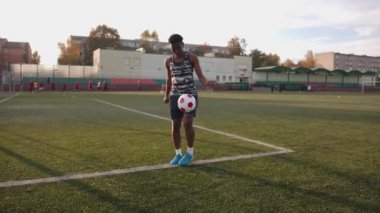 Kolsuz tişörtlü ve şortlu genç Afro-Amerikan kız futbol sahasında antrenman yapıyor ve kalenin yanında topu hokkabazlık yapıyor