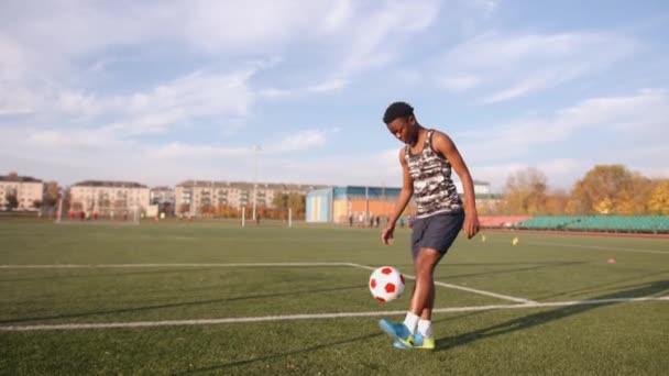 En ung svart flicka tränar i en stad stadion och jonglerar en fotboll från ena foten till den andra. Långsamma rörelser — Stockvideo