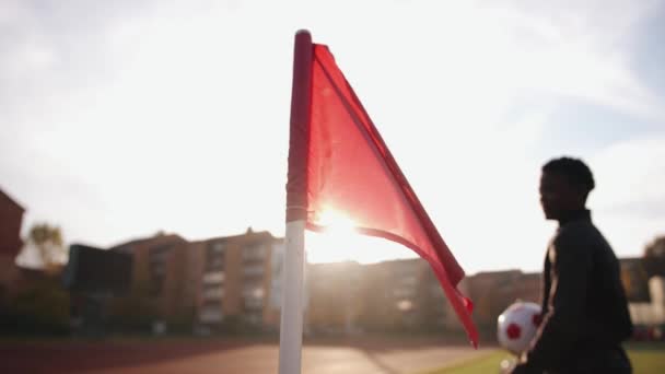 足球场上的一面红旗，在阳光的映衬下，一个年轻的黑人姑娘从他身边走过，手里拿着一个球。慢动作 — 图库视频影像