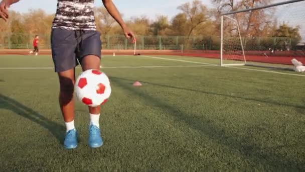 En trevlig ung svart tjej i ett fotbollslag träningspass står nära målet och jonglerar bollen. Långsamma rörelser — Stockvideo