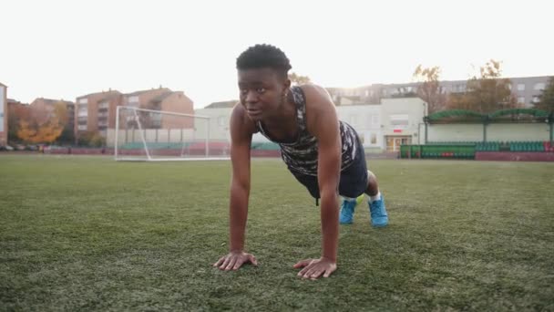 Ung svart flicka tränar på fotbollsplanen och står i en push up position på ena armen. Idrott och aktiv livsstil — Stockvideo