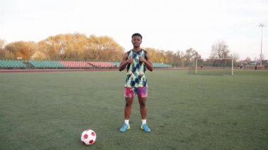 Kendine güvenen genç siyah kız topun yanındaki futbol sahasında duruyor ve her şey yolunda görünüyor.